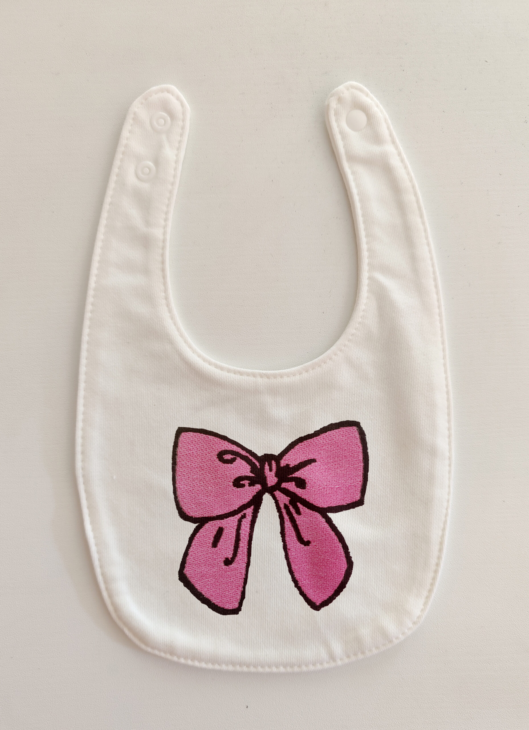 Fotografia di un bavaglino bianco con un fiocco rosa ricamato.
