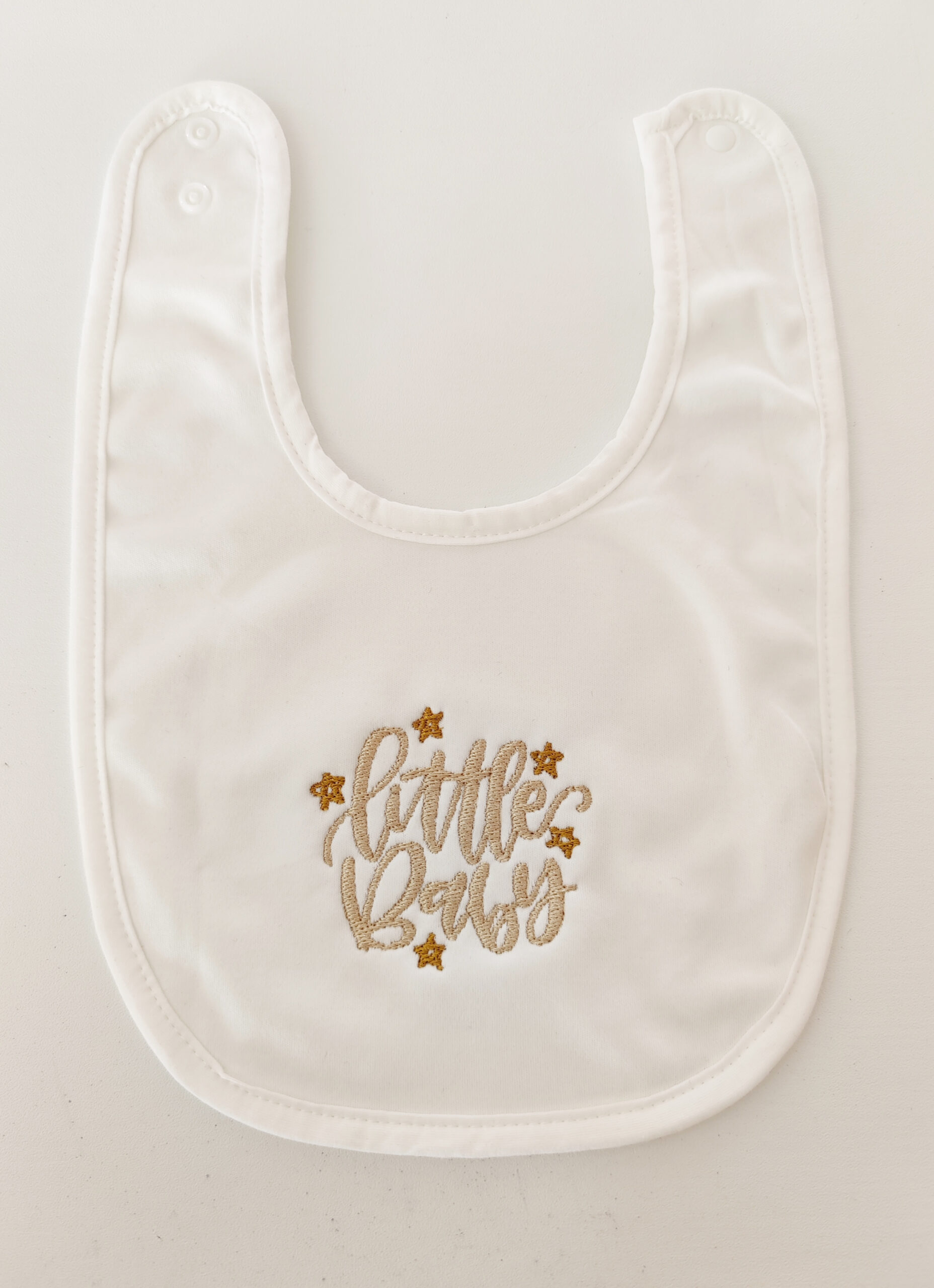 Fotografia di un bavaglino per neonato bianco con sopra ricamato "Little Baby" con delle stelle.
