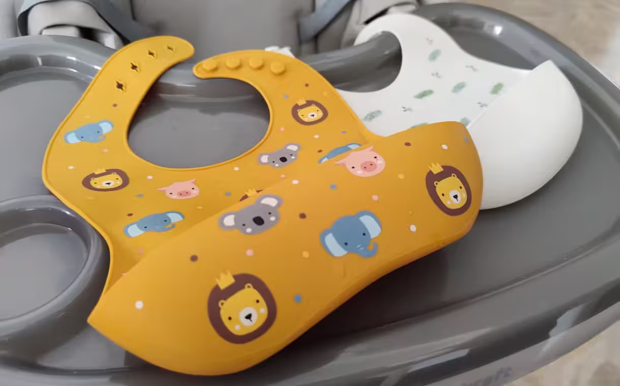 Fotografia di due bavaglini per la dentizione in silicone appoggiati su un seggiolone grigio.