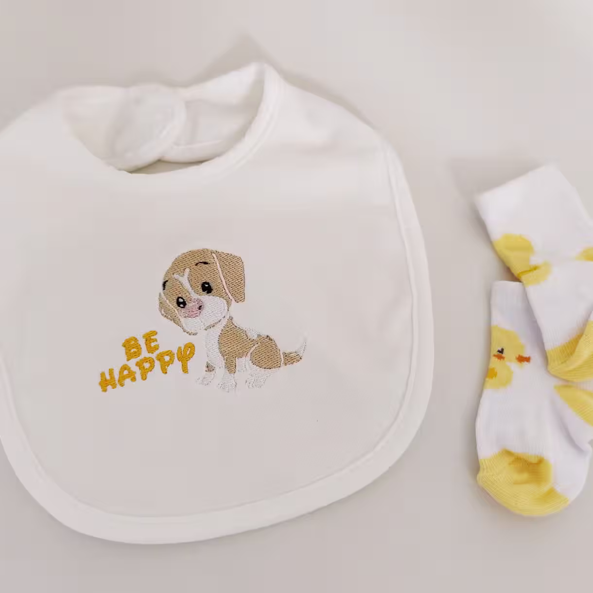 Fotografia di un bavaglino per neonato con il disegno di un cane con scritto accanto "Be Happy"