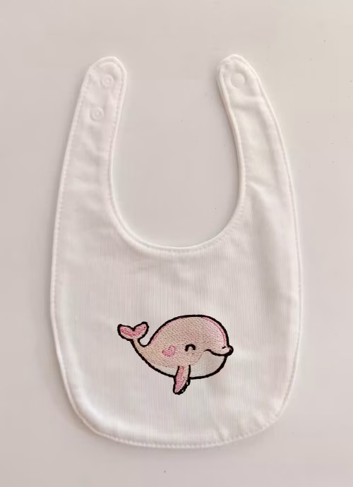 Fotografia di un bavaglino per neonato con una balena rosa ricamato sulla parte centrale.