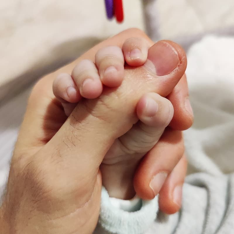 Fotografia di una mano di un neonato che stringe quella di un uomo.