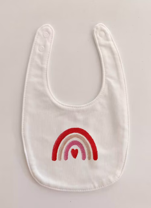 Fotografia di un bavaglino per neonato con un arcobaleno dalle sfumature rosa ricamato sulla parte centrale.