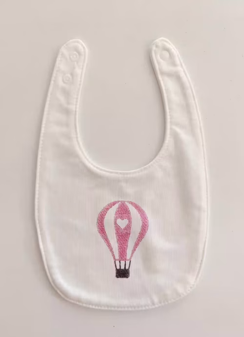 Fotografia di un bavaglino per neonato con una mongolfiera rosa ricamata sulla parte centrale.