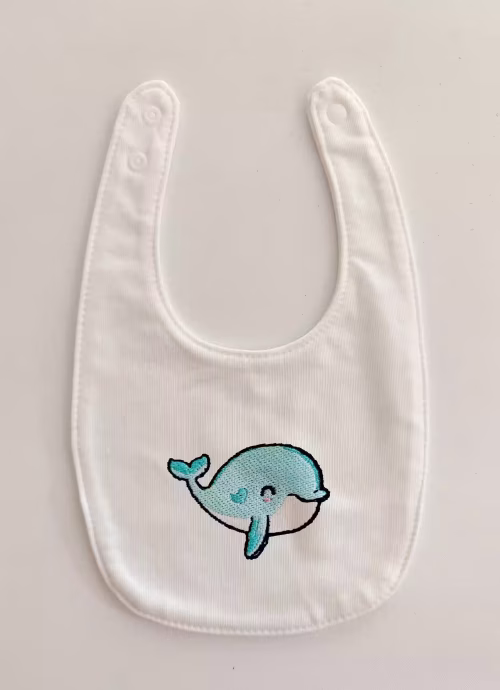 Fotografia di un bavaglino per neonato con una balena azzurra ricamata sulla parte centrale.